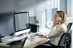 kobieta siedzi przy biurku z komputerem i rozmawia przez telefon