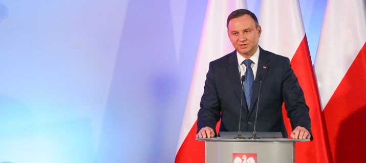 Prezydent Andrzej Duda przemawia przy mównicy. W tle - polskie flagi.