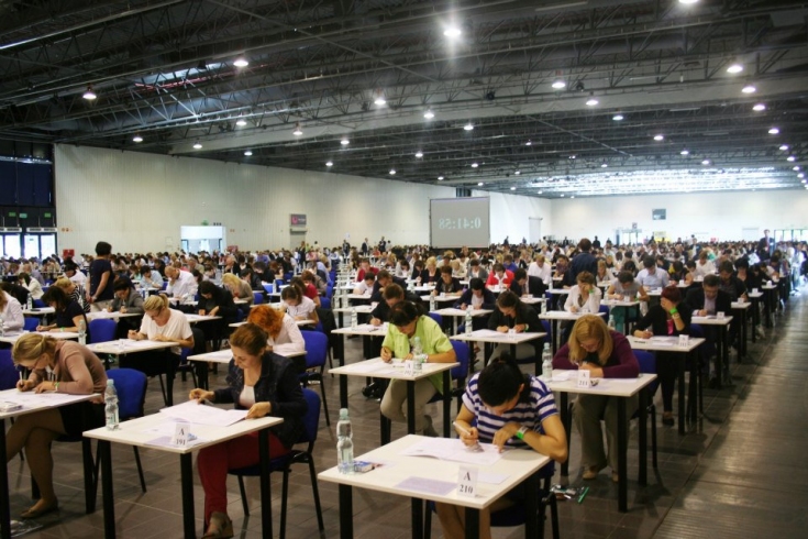 Uczestnicy siedzą w pojedynczych ławkach i piszą test