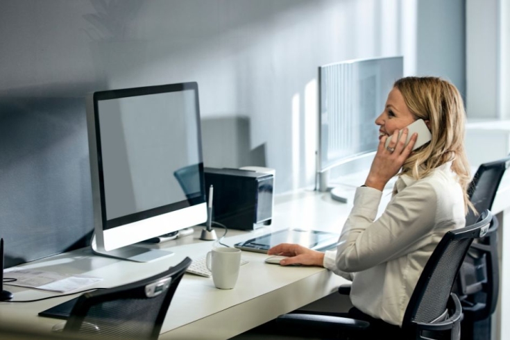 kobieta siedzi przy biurku z komputerem i rozmawia przez telefon