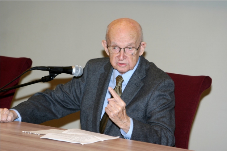 Profesor Zdzisław Sadowski podczas wykładu siedzi przy stole i mówi do mikrofonu.