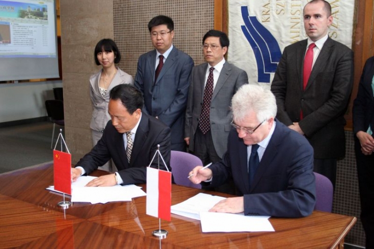 przedstawiciel delegacji Chin i Dyrektor KSAP siedza przy stole i podpisują dokumenty
