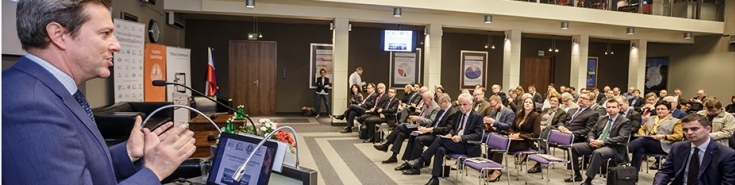 Mężczyzna stoi przy mównicy i przemawia do osób siedzących na Auli